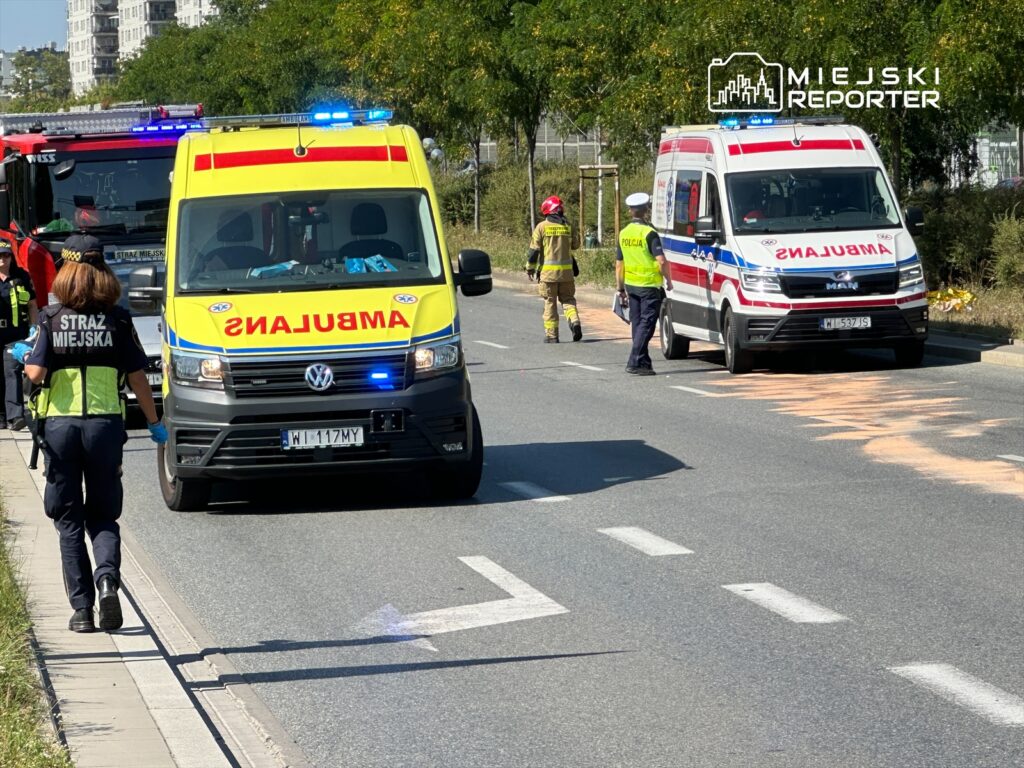 Na drodze stoją dwa ambulanse oraz pojazd straży pożarnej, a strażnik miejski zbiera informacje.