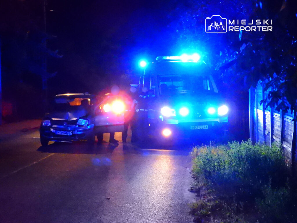 Policjanci rozmawiają z kierowcą przy uszkodzonym samochodzie na oświetlonej ulicy nocą.