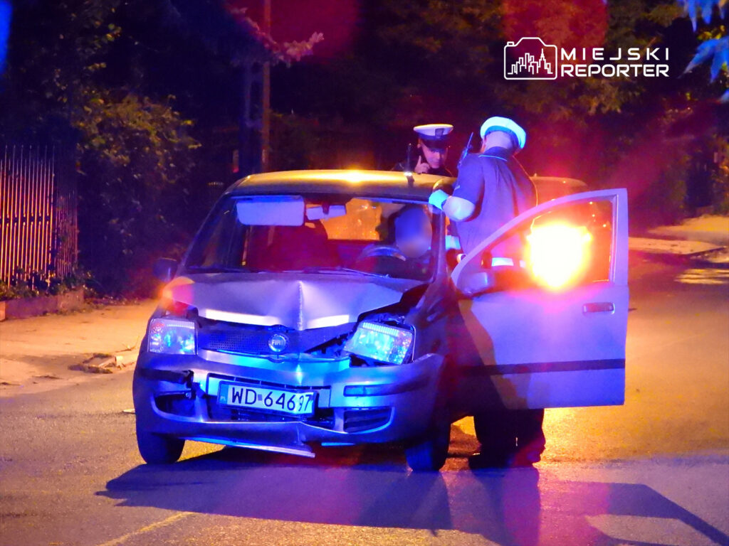 Policjanci przeprowadzają kontrolę w uszkodzonym samochodzie osobowym na oświetlonej ulicy.