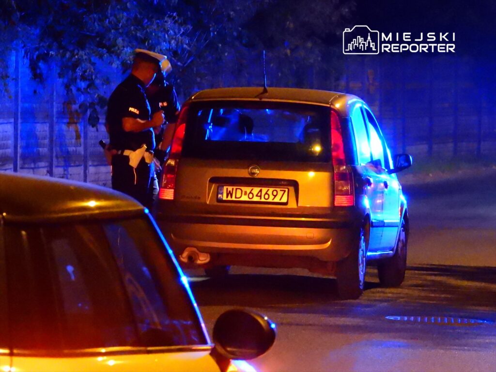 Policjant sprawdza dokumenty kierowcy w zatrzymanym samochodzie na oświetlonej niebieskimi światłami ulicy.
