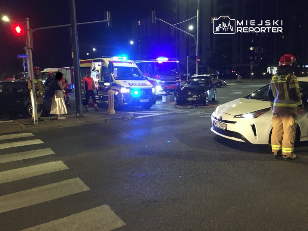 Na skrzyżowaniu w nocy, strażacy i ratownicy medyczni interweniują przy zderzeniu dwóch samochodów.