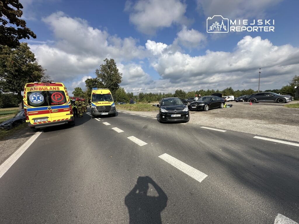 Na drodze stoją dwa ambulanse, a obok pracują ratownicy, w tle widać kilka zaparkowanych samochodów.