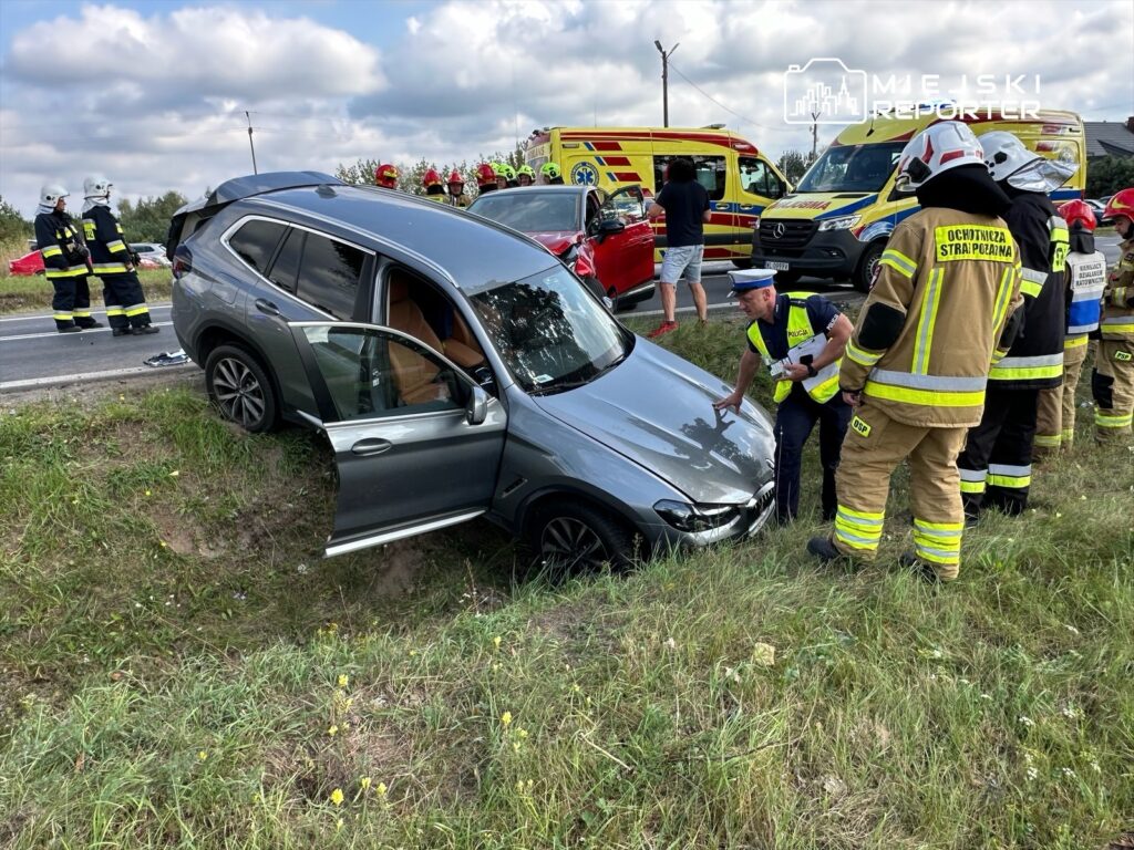 Kierowca w mundurze rozmawia z policjantem obok samochodu w rowie, podczas akcji ratunkowej z udziałem straży pożarnej.