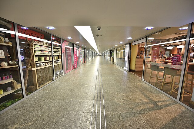 Pusty korytarz w nowoczesnym centrum handlowym z witrynami sklepów po obu stronach.