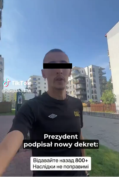 Mężczyzna w czarnej koszulce biega po osiedlu mieszkalnym, trzymając telefon w ręku i zwracając się do kamery. W tle nowoczesne budynki.