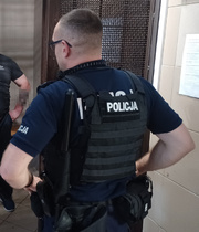 Funkcjonariusz policji w kamizelce kuloodpornej obserwujący otoczenie w zamkniętym pomieszczeniu.