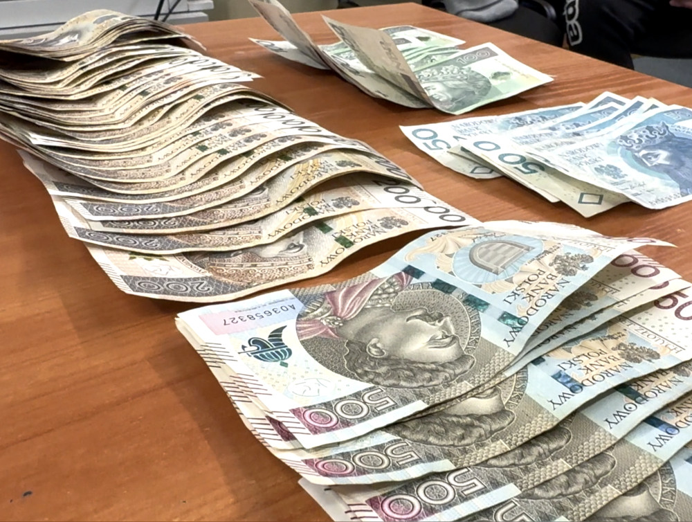 Stosy banknotów o nominale 100 i 500 zł leżą na drewnianym stole, tworząc uporządkowaną kompozycję.