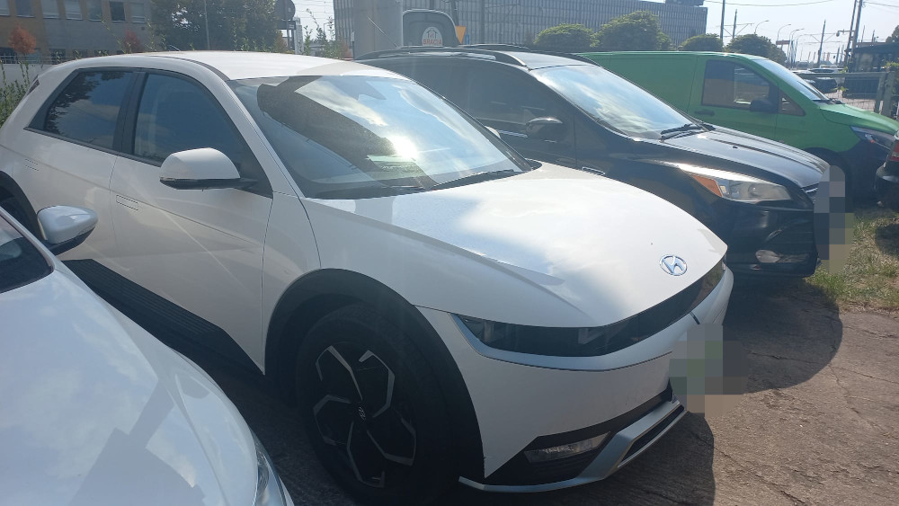 Nowoczesny, biały samochód elektryczny zaparkowany obok innych pojazdów na parkingu.