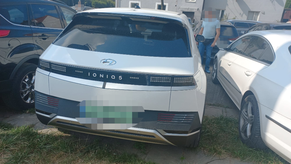 Nowoczesny samochód elektryczny Hyundai Ioniq 5 zaparkowany w wąskiej przestrzeni między innymi pojazdami.