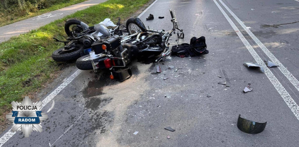 Motocykl leży na drodze, otoczony odłamkami szkła i częściami, w tle ścieżka rowerowa.