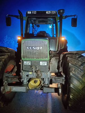 Traktor marki Fendt stojący na drodze w nocy, oświetlony niebieskim światłem.
