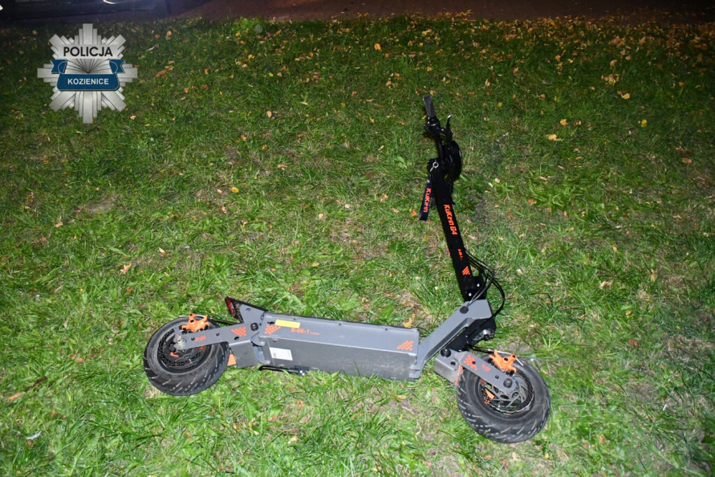 Złoty skuter elektryczny leży na trawie w nocy, obok widocznego fragmentu drogi.