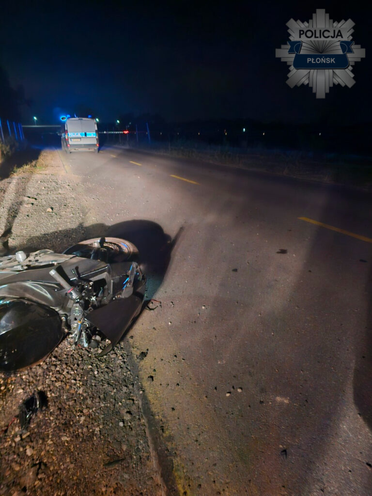 W nocy na drodze leży przewrócony motocykl obok radiowozu policyjnego. Otoczenie jest słabo oświetlone.