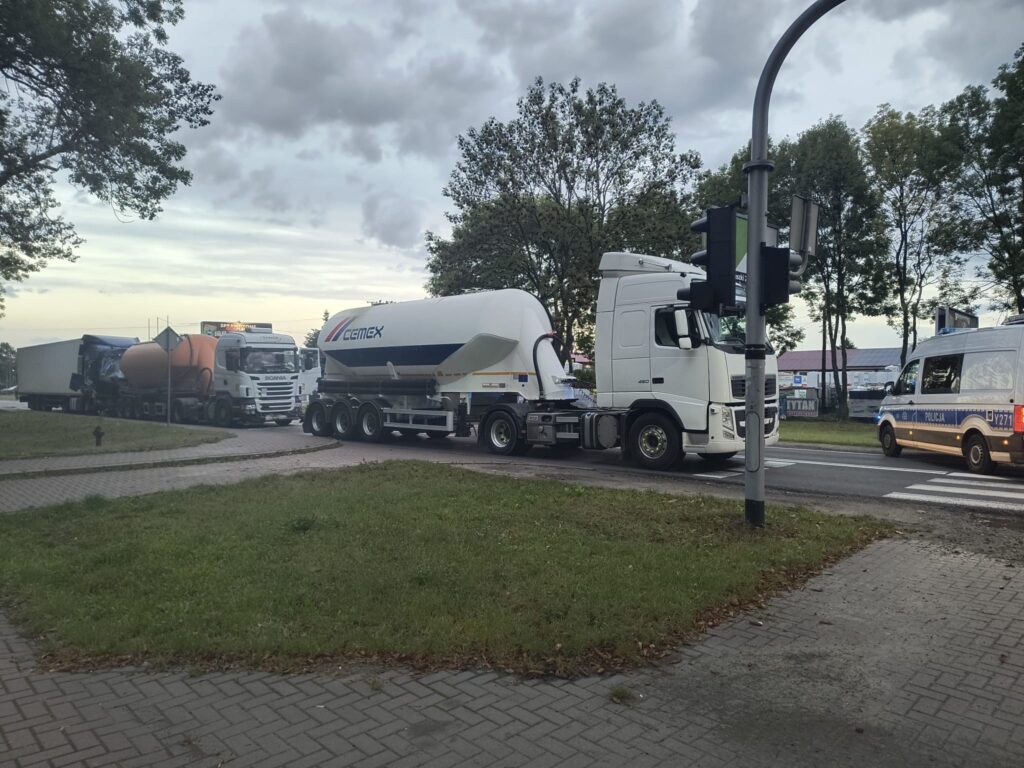 Kierowcy ciężarówek czekają na sygnalizację świetlną przy skrzyżowaniu, obok stoi radiowóz policyjny.
