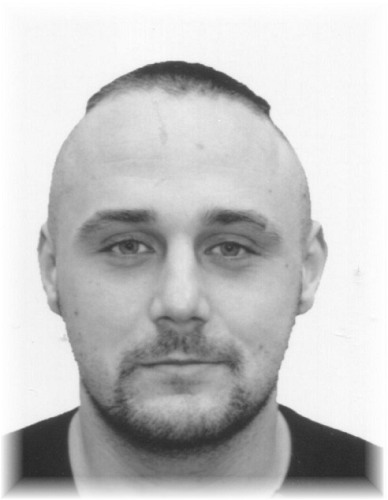 Mężczyzna z krótkimi włosami, gładko ogolonymi po bokach, patrzy prosto w obiektyw kamery.