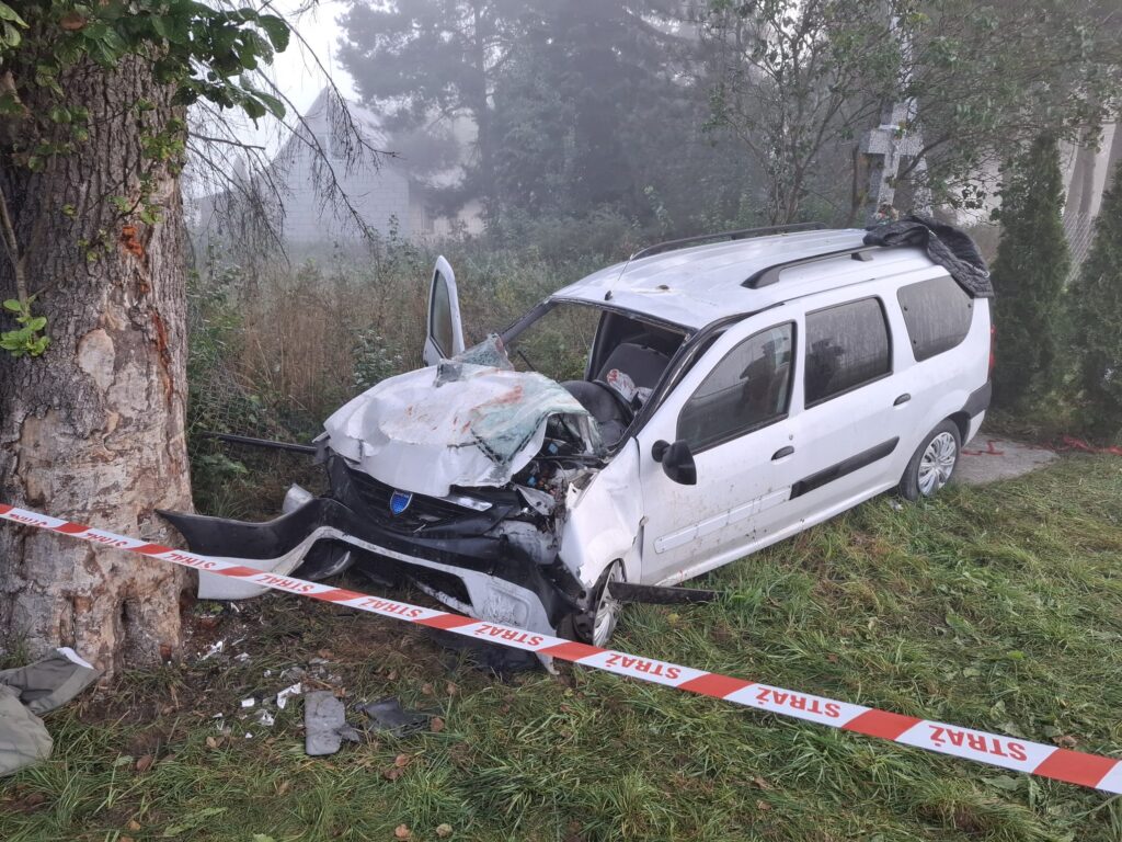 Rozbity samochód osobowy stoi przy drzewie, otoczony taśmą policyjną w mistycznej, porannej mgle.