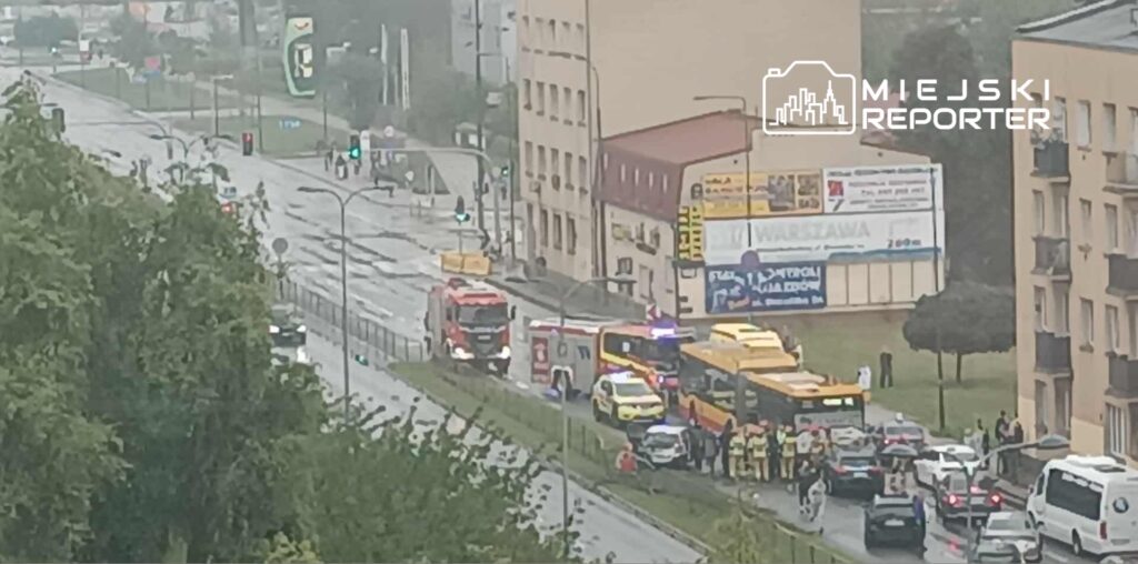 Na mokrej ulicy zatrzymane pojazdy ratunkowe oraz grupka ludzi obserwujących sytuację.