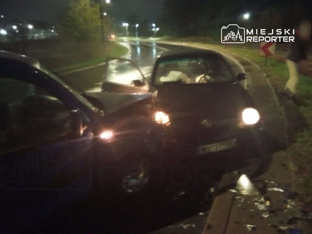 Zderzenie dwóch samochodów osobowych na mokrej drodze, w tle oświetlone lampami ulice nocą.
