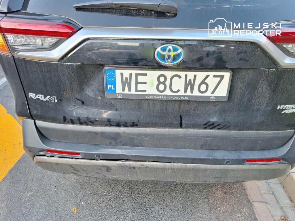 Czarny samochód Toyota RAV4 z widocznymi śladami brudu i uszkodzeniami na tylnym zderzaku, zaparkowany na ulicy.
