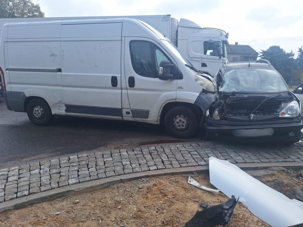 Biały furgon zderzył się z czarnym samochodem osobowym na skrzyżowaniu, obydwa pojazdy uszkodzone.