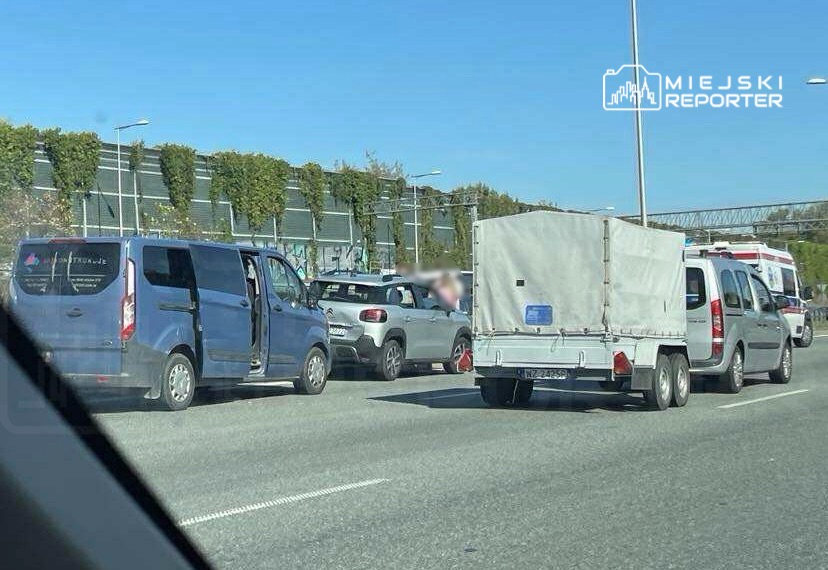 Zablokowany ruch drogowy spowodowany wypadkiem, kilka pojazdów zatrzymanych na jezdni w słoneczny dzień.