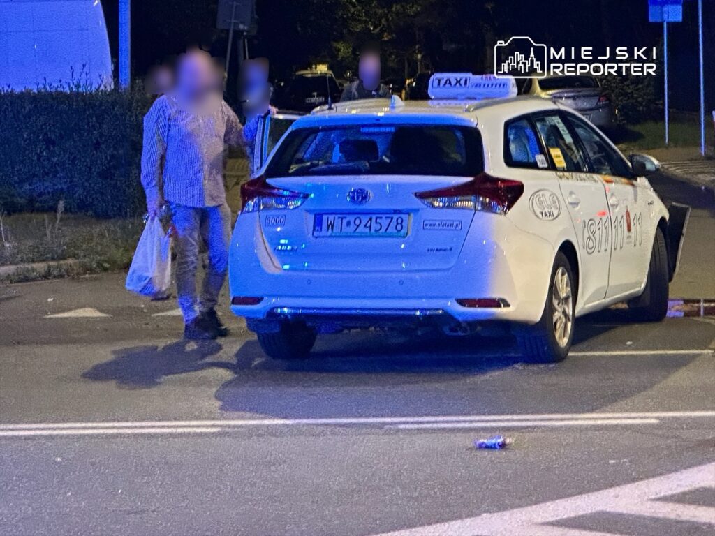 Mężczyzna w koszuli w kratkę trzymający torby przy taksówce zaparkowanej na ulicy w nocy.