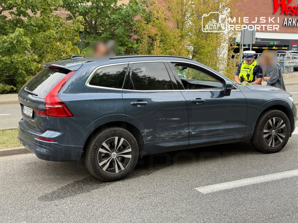 Nieoznakowany radiowóz policyjny rozmawia z kierowcą uszkodzonego SUV-a na ulicy, w pobliżu zieleni.