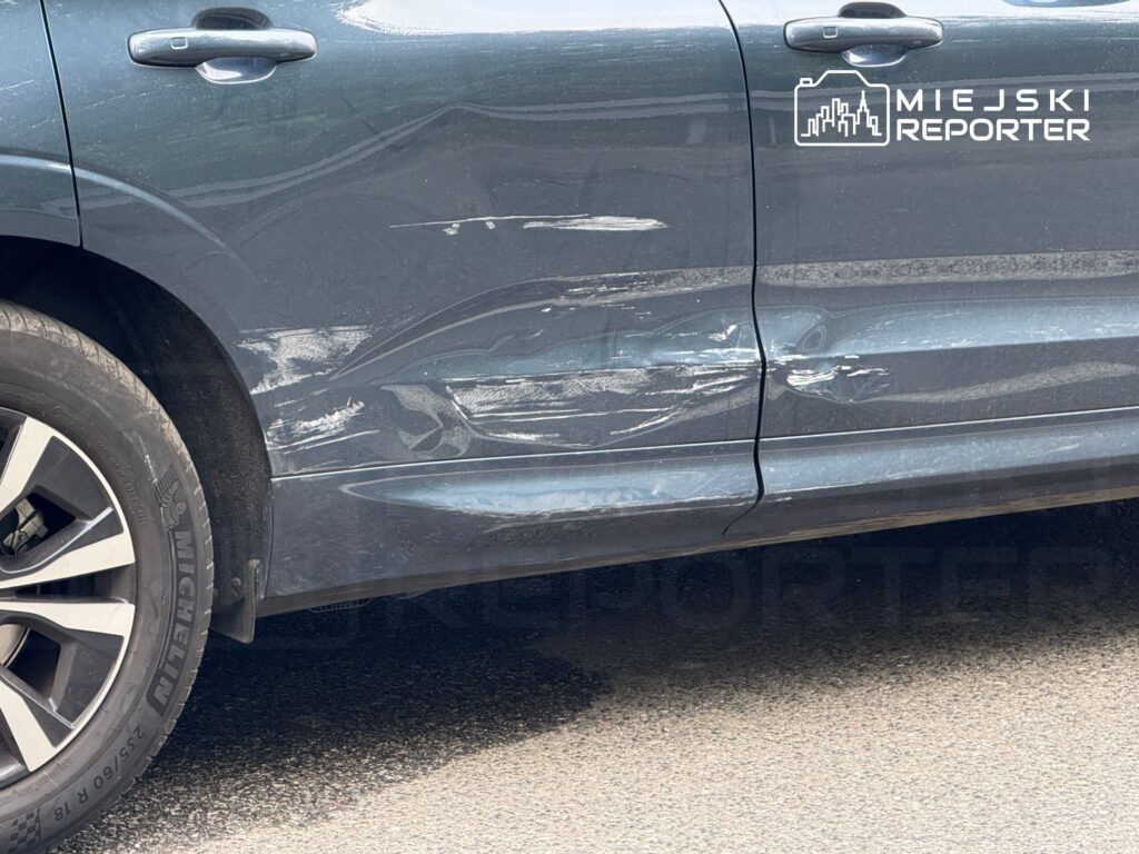 Zarysowany bok ciemnego SUV-a z widocznymi śladami uszkodzeń na drzwiach.