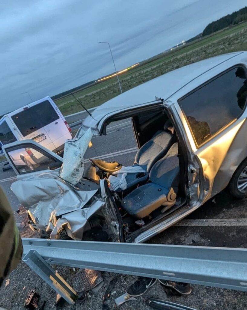 Uszkodzony samochód osobowy z wgniecioną stroną, stojący na drodze obok bariery ochronnej.