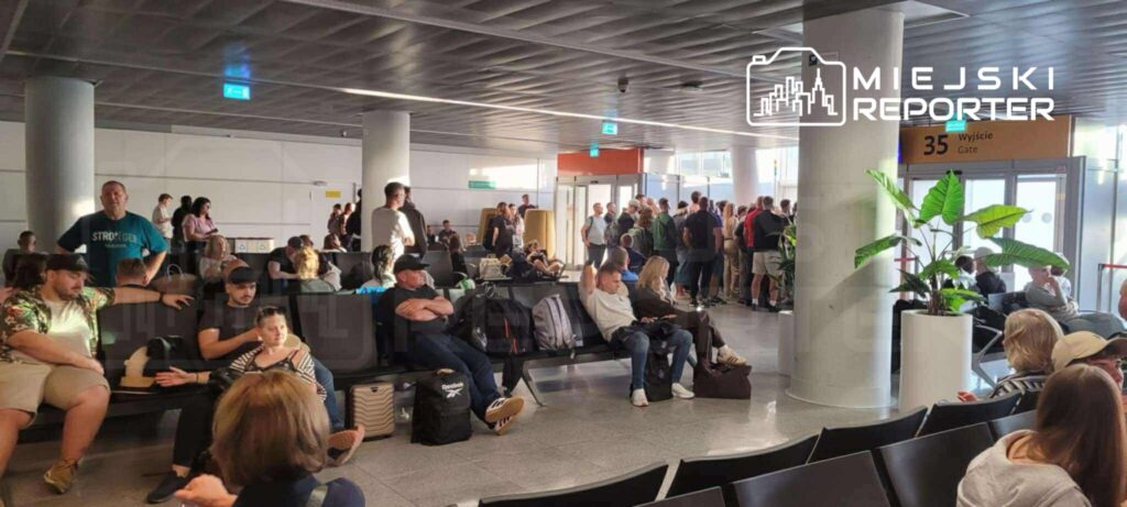 Grupa pasażerów czeka w terminalu lotniska, niektórzy siedzą, inni stoją w kolejce przy wyjściu 35.