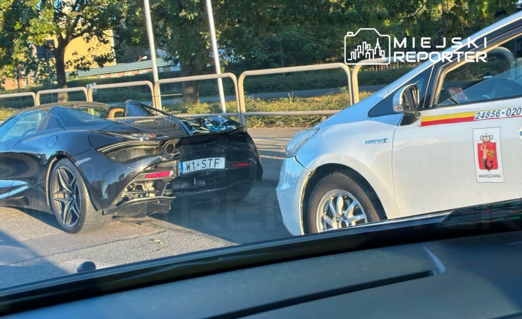 Czarny samochód sportowy zaparkowany obok białego taxi na miejskiej ulicy w słoneczny dzień.