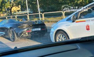 Czarny samochód sportowy zaparkowany obok białego taxi na miejskiej ulicy w słoneczny dzień.