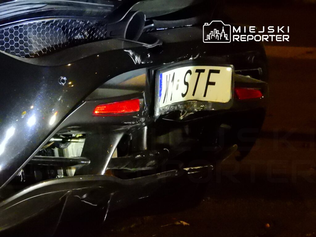 Uszkodzony tył czarnego sportowego samochodu z widocznym zarysowaniem i uszkodzeniem zderzaka, nocą.