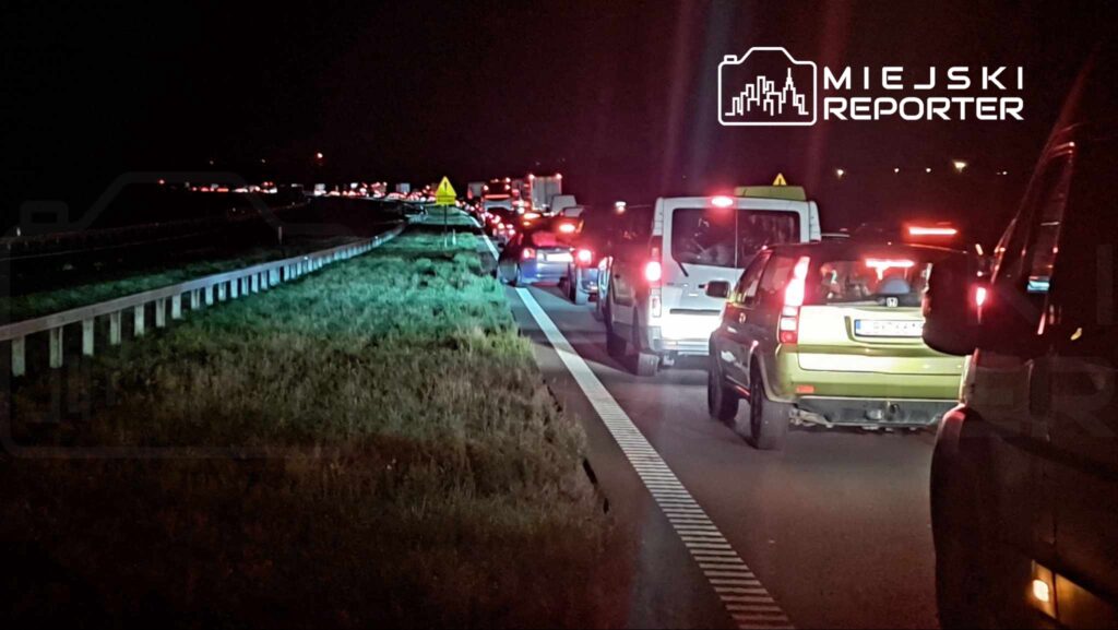 Korki na drodze, samochody stojące w nocy, oświetlone przez światła pojazdów.