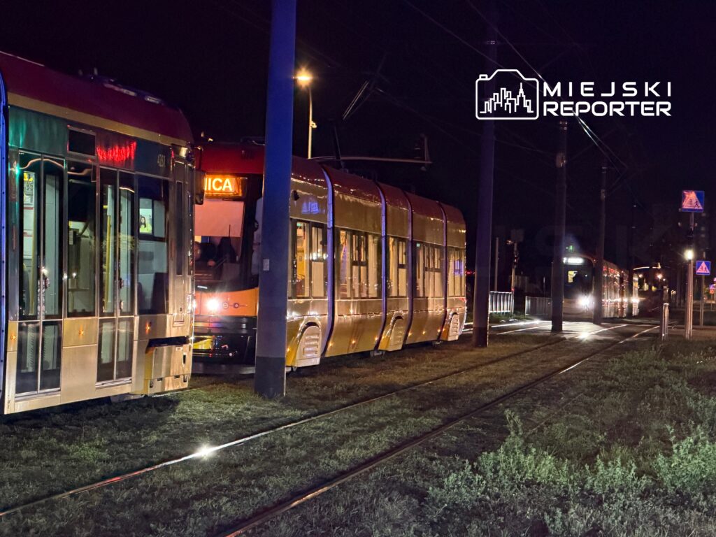 Tramwaje zatrzymane na nocnym przystanku, oświetlone przez latarnie, z wyraźnymi refleksami na szkle.