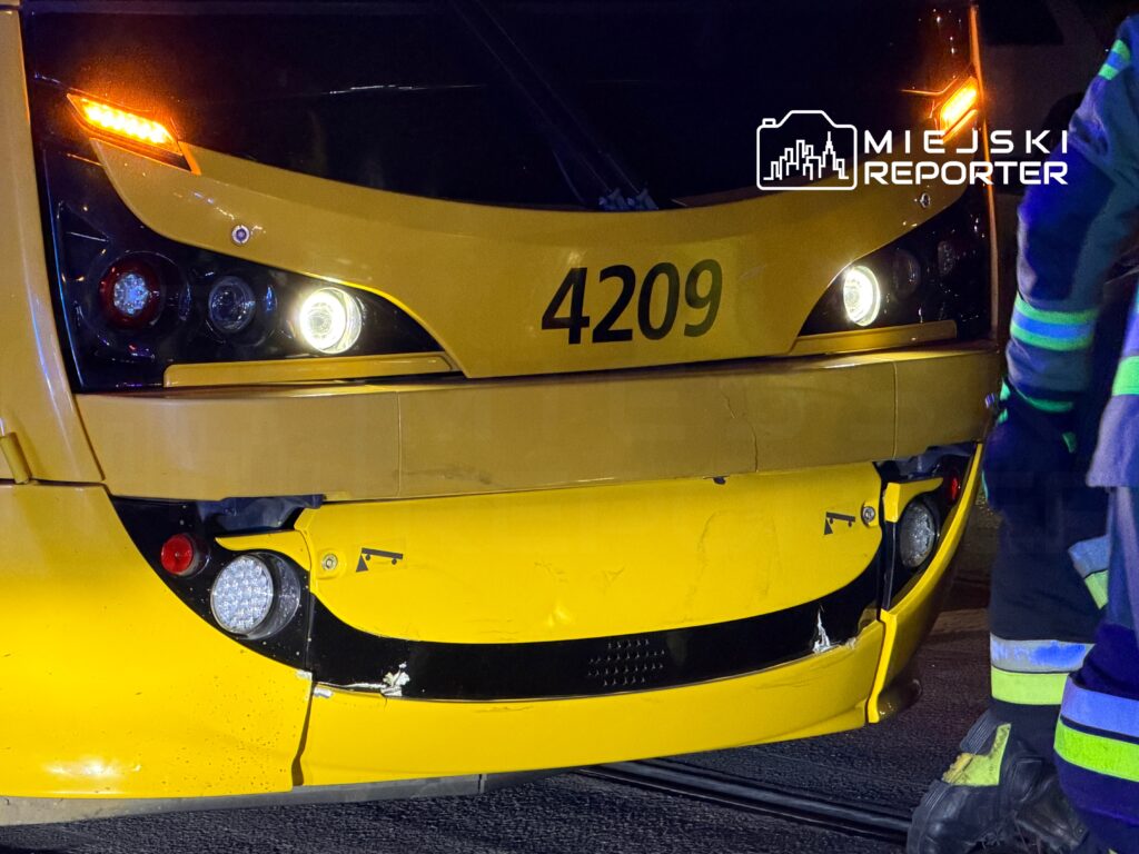 Żółty tramwaj z uszkodzoną przednią częścią stoi na torach, obok niego pracownik w mundurze ratunkowym.