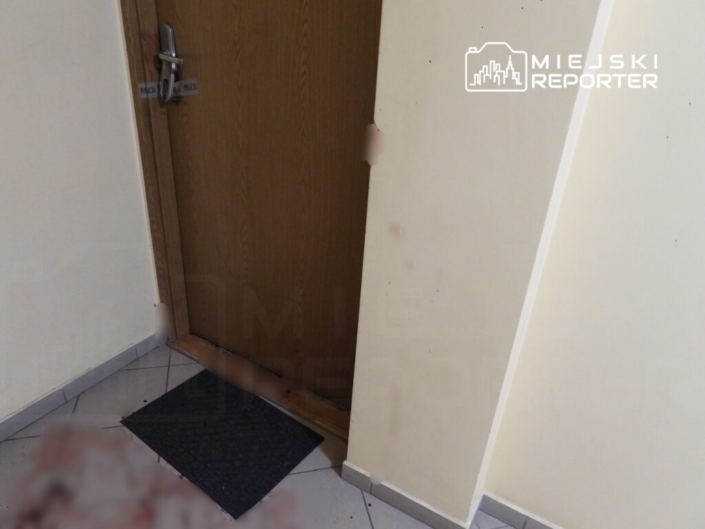 Drzwi w kolorze brązowym z zamkiem i napisem "POLICJA" oraz do matowy wycieraczka na podłodze, w otoczeniu jasnych ścian.