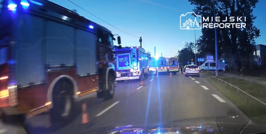 W nocy na ulicy stoją samochody straży pożarnej i karetki, włączone są sygnały świetlne.