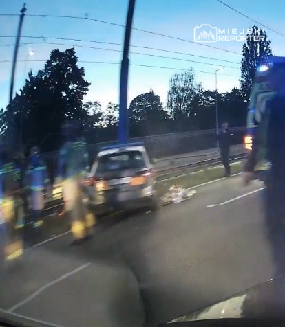 Ratownicy medyczni udzielają pomocy poszkodowanemu przy samochodzie na drodze.