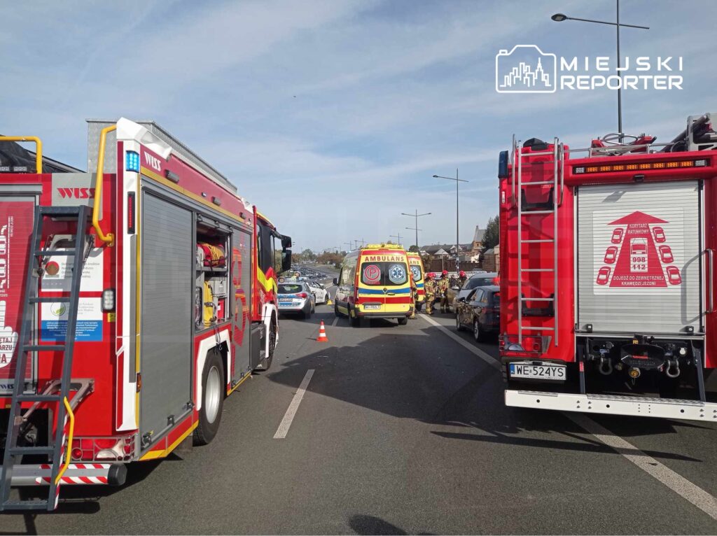 Na jezdni zatrzymane pojazdy ratunkowe, w tym wóz strażacki i ambulans, podczas akcji ratunkowej.