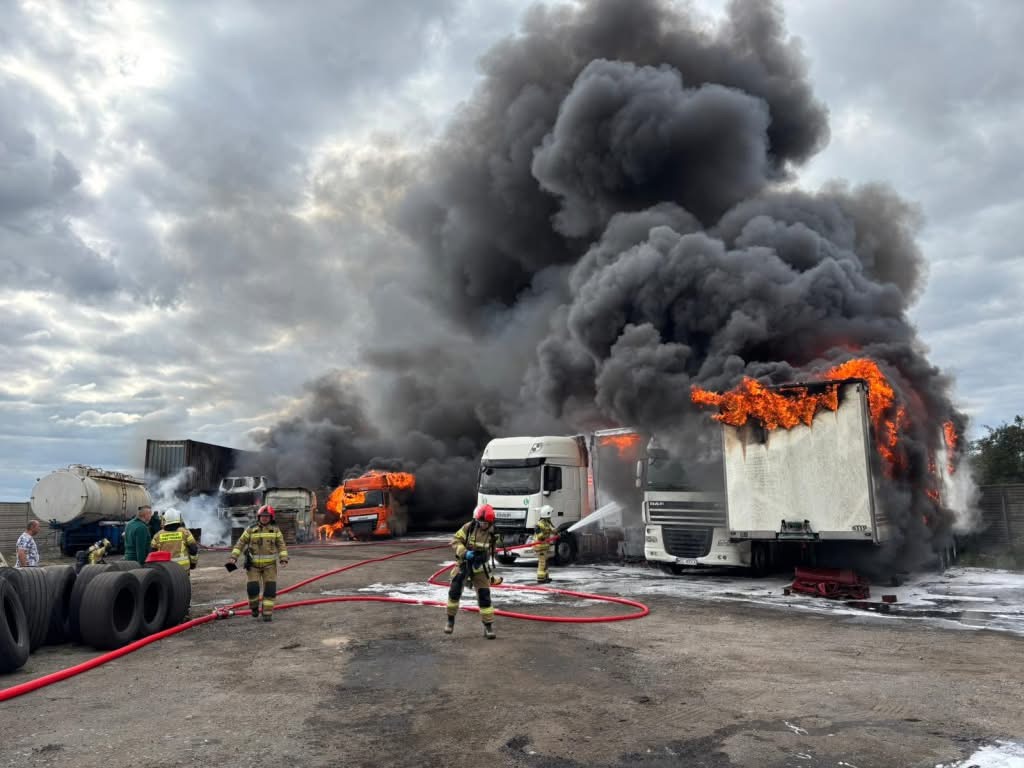 Strażacy gaszą płonące ciężarówki w obszarze przemysłowym, otoczeni gęstym dymem i ogniem.