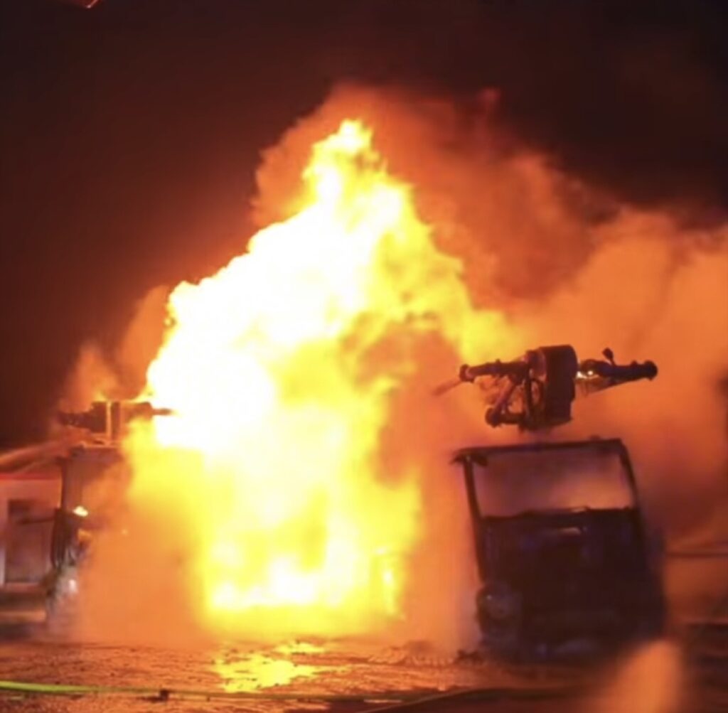 Pojazd z zamontowaną bronią wybucha w płomieniach, otoczony chmurą dymu w ciemnej scenerii nocnej.