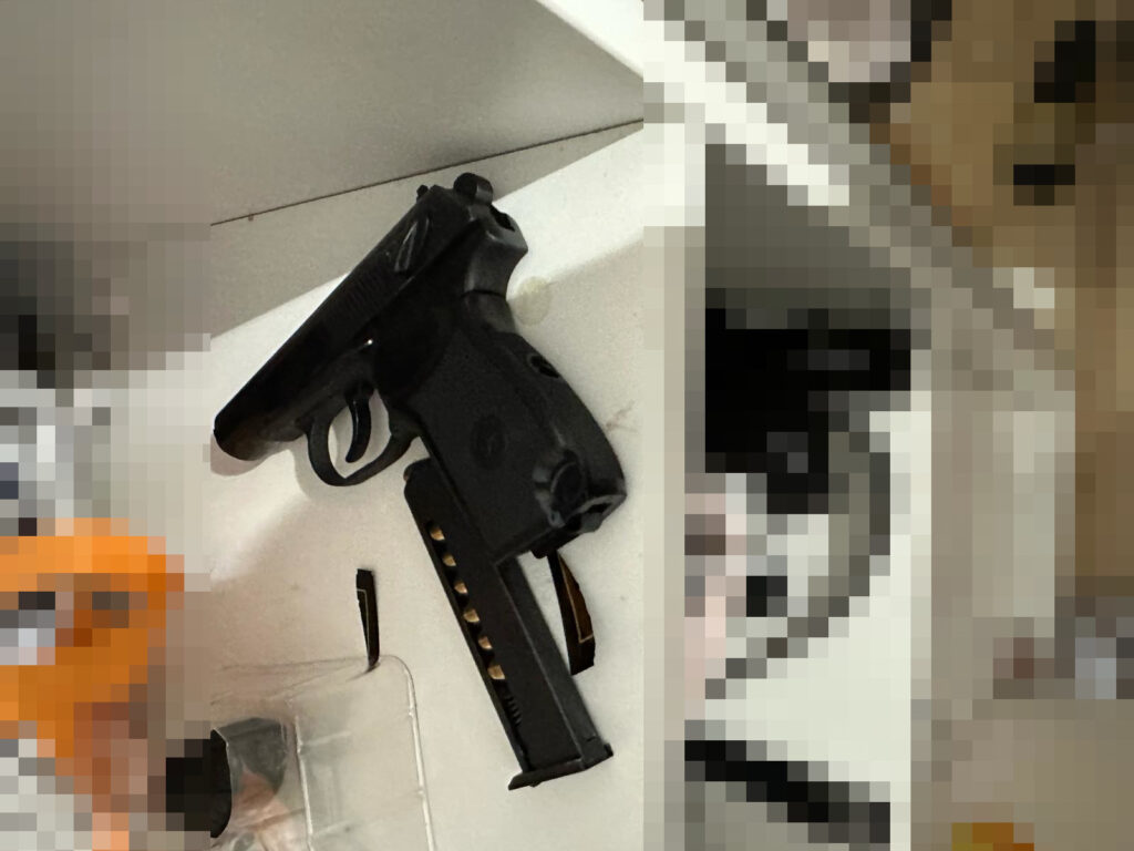 Pistolet leżący na białej półce obok magazynka i innych przedmiotów.
