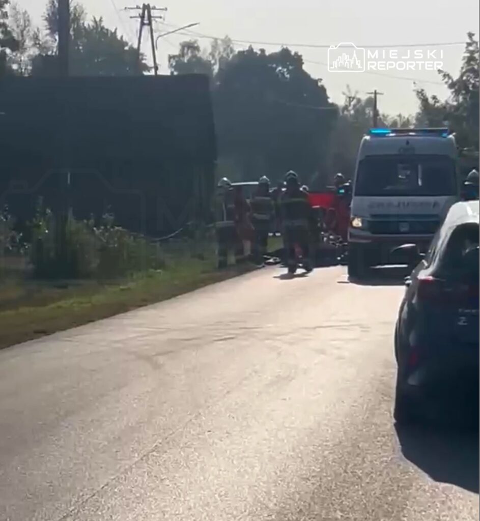 Grupa strażaków i ratowników medycznych pracuje przy wypadku drogowym na wiejskiej drodze.