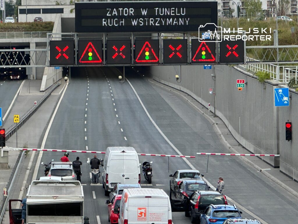Zatrzymany ruch w tunelu, sygnalizacja świetlna w kolorze czerwonym, widoczne samochody czekające na wjazd.