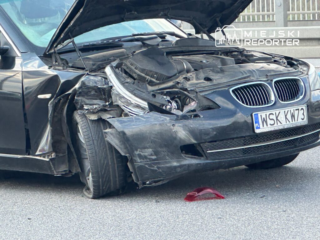 Czarny samochód osobowy z uszkodzoną przednią częścią, stojący na drodze z otwartą maską.