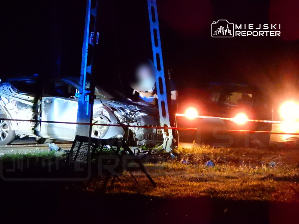 Uszkodzony samochód osobowy stoi przy drodze, obok interweniujący policjanci w nocy.