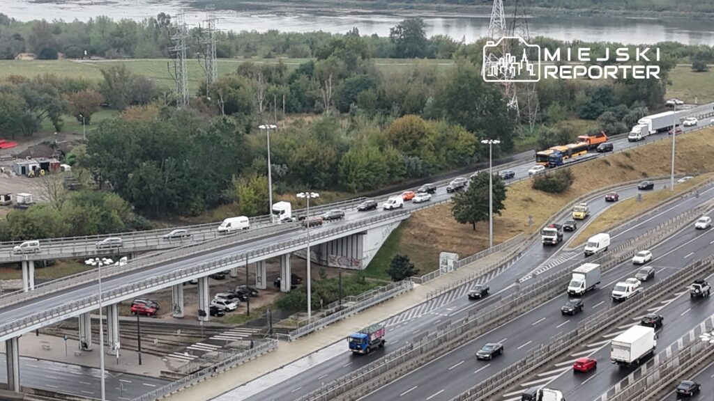 Ruch samochodowy na dwupoziomowej drodze z widokiem na zieleń i rzekę w tle.