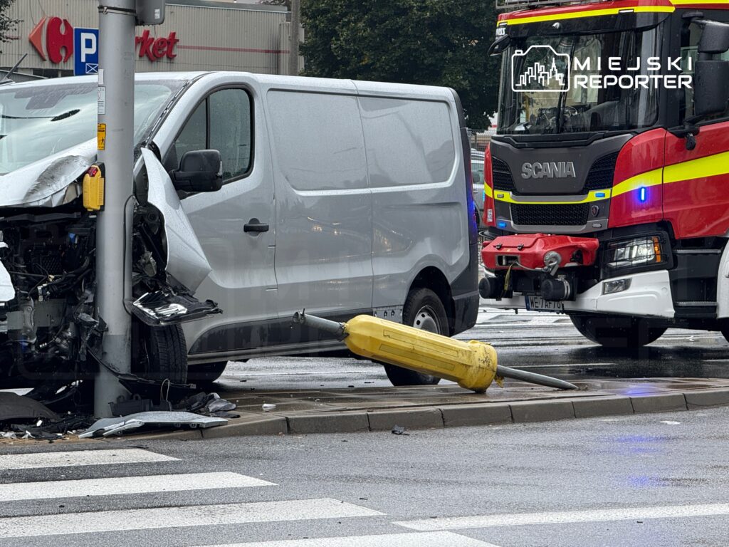 Zniszczony furgonetka uderzona w latarnię na skrzyżowaniu, obok widoczny wóz strażacki.