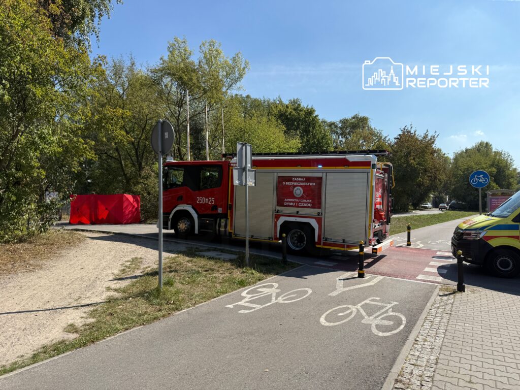 Czerwony wóz strażacki stoi obok drogi rowerowej, obok widoczny jest czerwony namiot zabezpieczający.